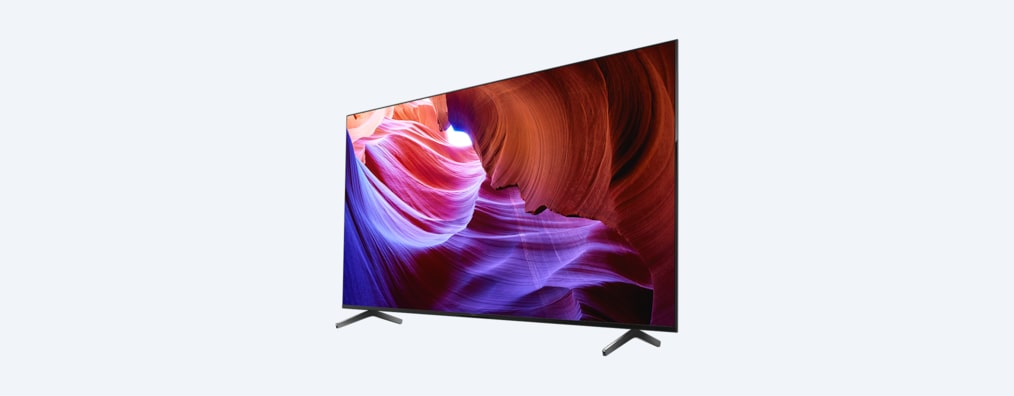 Телевизор BRAVIA X85K с подставкой и изображением фиолетовых и оранжевых объектов на экране, вид под углом