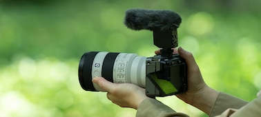 Изображение использования, на котором показан вид слева камеры в руках пользователя с прикрепленным микрофоном и ветрозащитой
