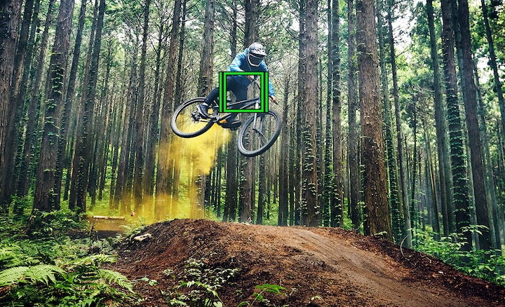 Человек на горном велосипеде в прыжке на лесной тропе с зеленым квадратом, указывающим на работу функции отслеживания в режиме реального времени