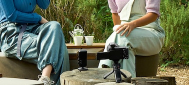 Изображение двух людей, сидящих на улице, перед ними находится микрофон, а рядом стоит камера с прикрепленным приемником