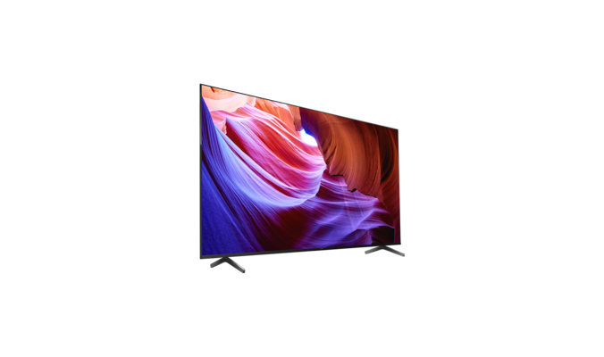 Телевизор BRAVIA X85K с подставкой и изображением фиолетовых и оранжевых объектов на экране, вид под углом