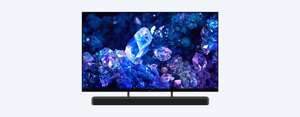 Телевизор BRAVIA A90K с изображением синих и фиолетовых кристаллов на экране и саундбар, вид с угла спереди
