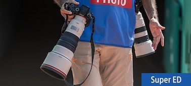 Изображение продукта в использовании, на котором фотограф мужского пола несет две камеры с телеобъективами