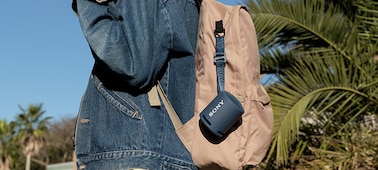 Изображение портативной беспроводной акустической системы XB13 EXTRA BASS(TM), прикрепленной к рюкзаку молодой девушки.