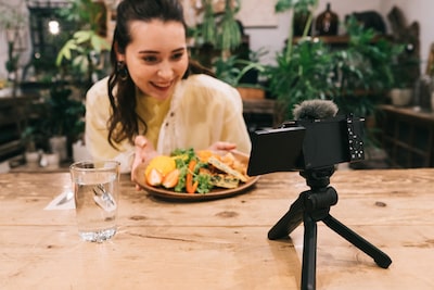 Изображение женщины с тарелкой еды, сидящей за столом перед камерой, установленной на мини-штативе