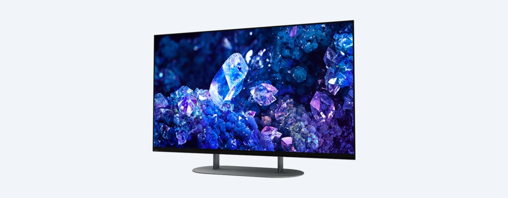 Телевизор BRAVIA A90K с изображением синих и фиолетовых кристаллов на экране и подставка, вид с угла спереди