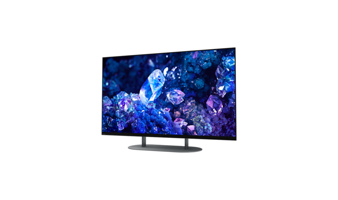 Телевизор BRAVIA A90K с изображением синих и фиолетовых кристаллов на экране и подставка, вид с угла спереди