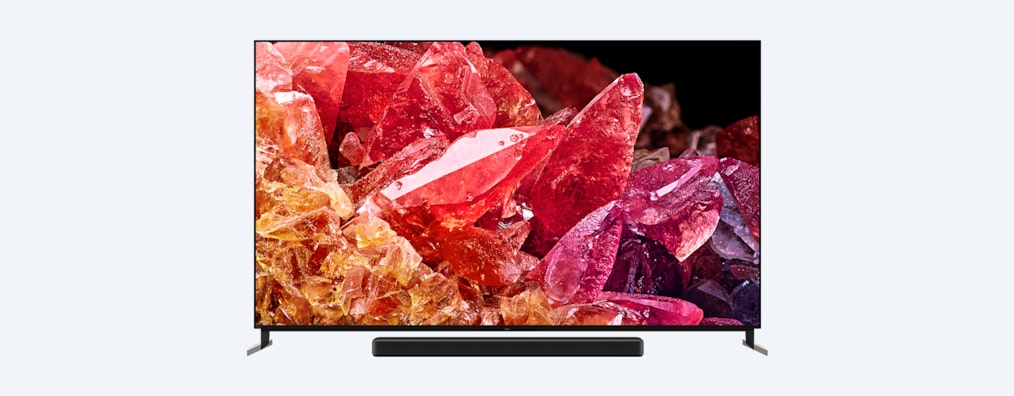 Телевизор BRAVIA X95K на подставке с саундбаром и изображением красных и оранжевых кристаллов на экране, вид спереди