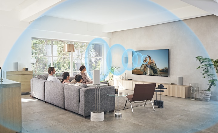 Сидящая на диване семья смотрит телевизор с домашним кинотеатром HT-A9, установленный на деревянной полке, а от экрана расходятся звуковые волны.