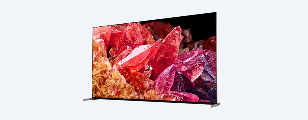 Телевизор BRAVIA X95K на подставке и с изображением красных и оранжевых кристаллов на экране, вид с угла