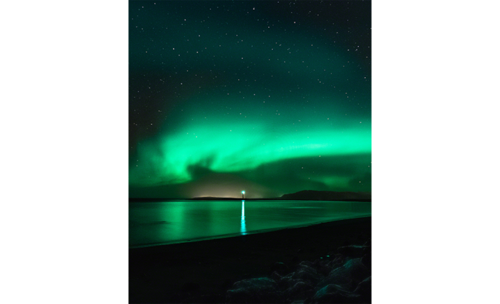 Ночной снимок изумрудного северного сияния на темном небе над маяком и морем