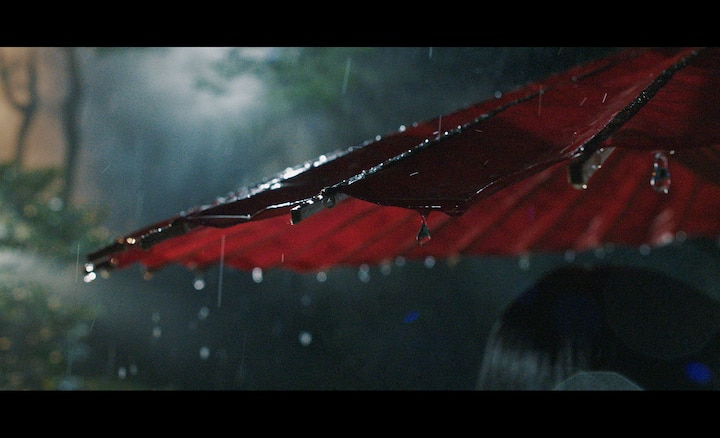 Снимок капель дождя, падающих с красного зонтика, сделанный в условиях низкой освещенности