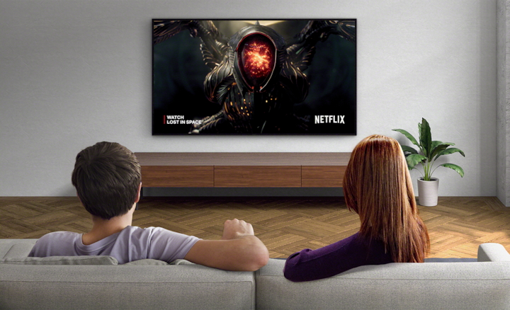 Два человека смотрят телевизор со снимком экрана из сериала «Затерянные в космосе» и логотипом Netflix справа внизу