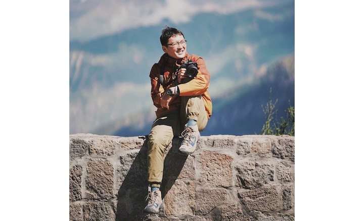 Портрет фотографа Ли Сяна, сидящего на камне с камерой в руках