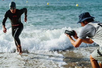 Изображение продукта в использовании, на котором мужчина держит камеру, чтобы снять триатлониста, выбегающего из моря