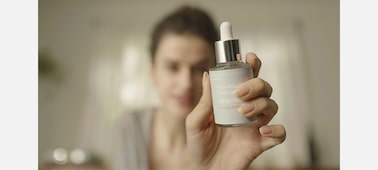 Изображение женщины, рассматривающей продукт для макияжа в своей руке