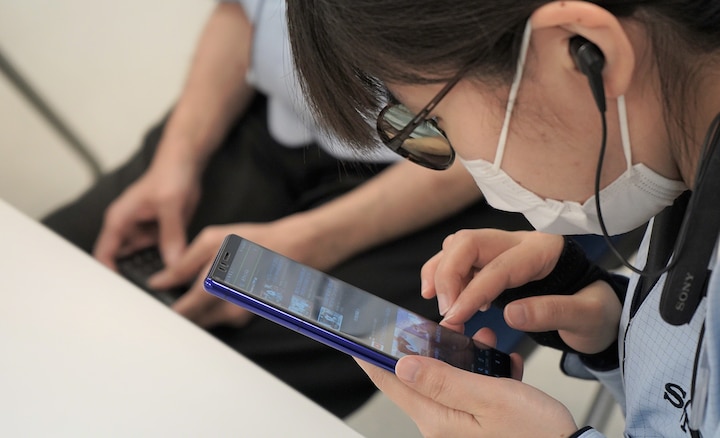 Девушка в очках, маске и наушниках от Sony с очень близкого расстояния смотрит на дисплей Xperia