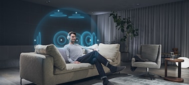 Мужчина сидит на диване в гостиной и слушает музыку в наушниках, используя беспроводной передатчик