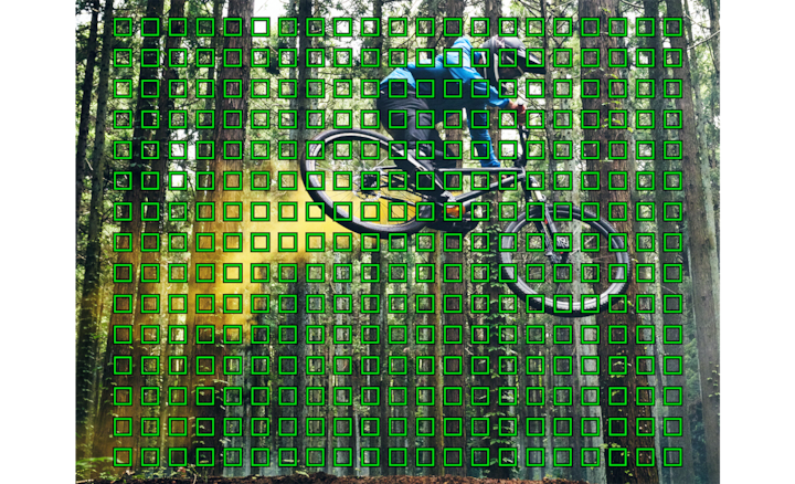 Изображение человека на горном велосипеде в лесу, на которое наложено несколько зеленых квадратов, представляющих точки автофокусировки