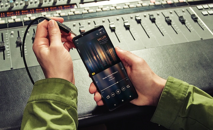 Крупный план человека за микшером, который вставляет штекер для наушников в аудиоразъем 3,5 мм смартфона Xperia