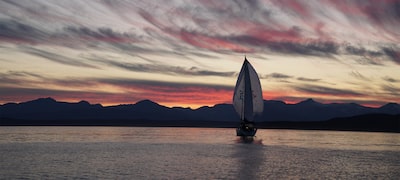Изображение парусной лодки на озере на фоне заката, текстурного неба и темных холмов