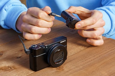 Человек использует кабель, чтобы подключить устройство ECM-W2BT к совместимой камере через стереофонический мини-разъем 3,5 мм