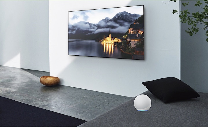Изображение гостиной с телевизором на стене и устройством с поддержкой Alexa сбоку