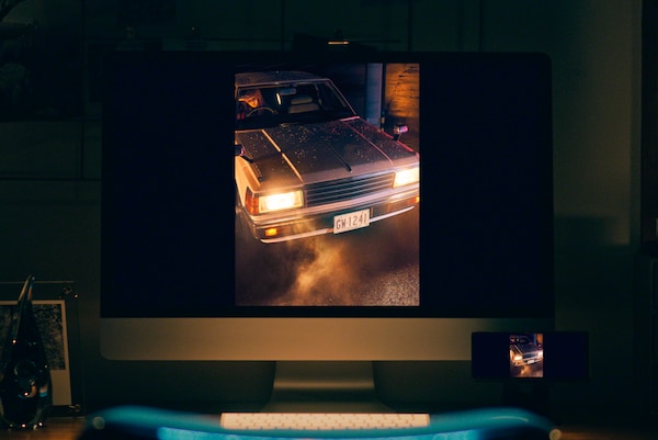 Настольный компьютер, на мониторе которого изображение автомобиля с включенными фарами, с низкой освещенностью