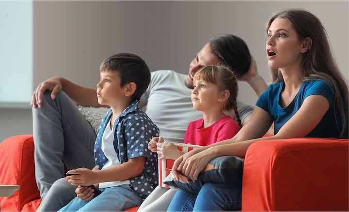 Мужчина и женщина с двумя детьми на диване смотрят телевизор