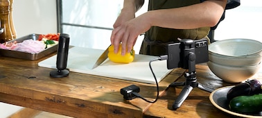 Изображение, на котором показан человек, готовящий еду, рядом с которым стоит микрофон с приемником, подключенным к смартфону на стойке через кабель USB