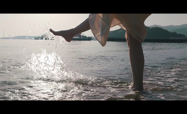Женщина на пляже, плещущая ногами в воде.