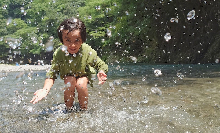Девочка, которая играет в ручье и брызгает водой на камеру