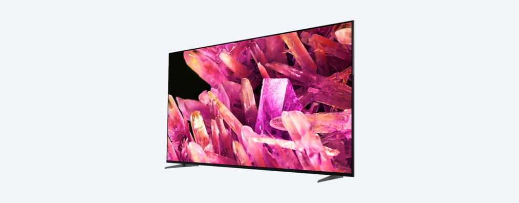 Телевизор BRAVIA X90K на подставке с изображением розовых кристаллов на экране, вид спереди под углом