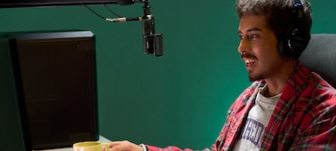 Изображение мужчины, который сидит перед экраном монитора ПК в наушниках, подключенных с помощью кабеля к микрофону