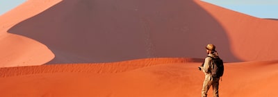 Изображение человека, смотрящего в сторону от камеры, на фоне красных песчаных дюн