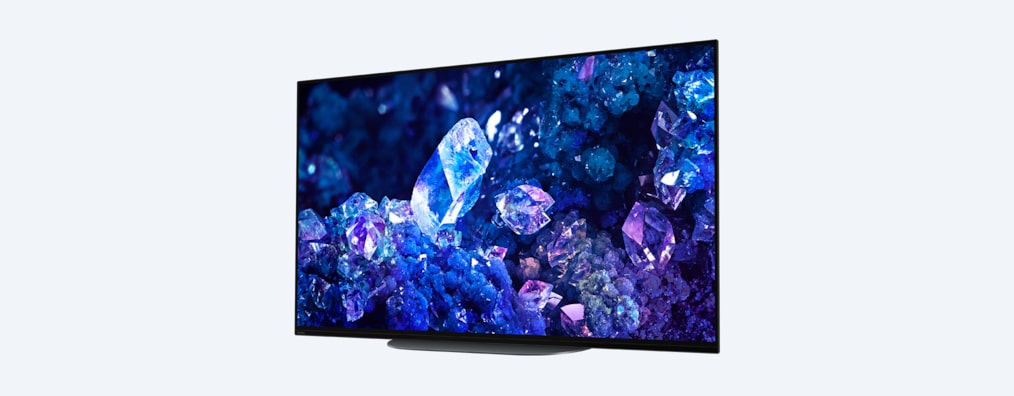 Телевизор BRAVIA A90K с изображением синих и фиолетовых кристаллов на экране, вид с угла спереди