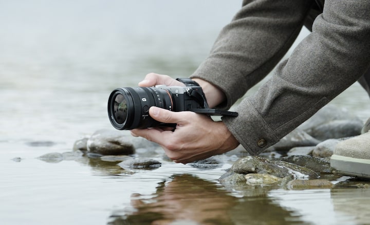 Изображение пользователя, держащего камеру α7C II с объективом FE 24–50 мм F2.8 G у водного полотна реки. Пользователь ведет съемку снизу