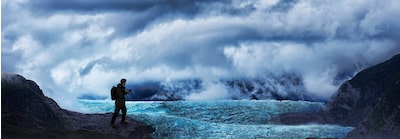 Изображение, показывающее пользователя с камерой в руках в дикой горной среде; вокруг него туман, облака и ледяное поле