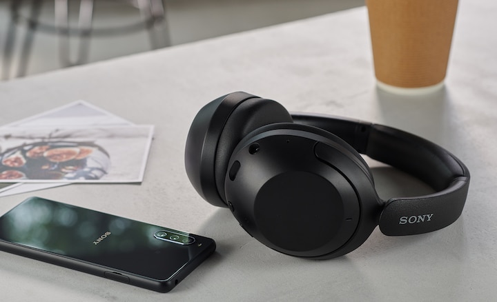 Черные наушники WH-XB910N на столе рядом с чашкой кофе и смартфоном