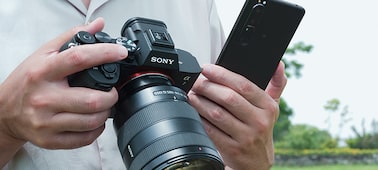 Фотография человека, который держит в руках Alpha 7 IV и смартфон, чтобы отправить фотографии или видео сразу после съемки