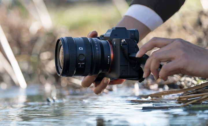 Изображение пользователя, держащего камеру α7 IV с объективом FE 16–25 мм F2.8 G у водного полотна реки. Пользователь ведет съемку снизу